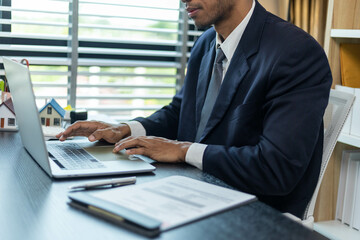 A man in a suit is typing on a laptop at a desk. Concept of professionalism and focus, as the man is dressed in a business suit and he is working on important tasks. The presence of the laptop
