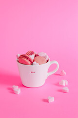Valentine's day card with a copy space. Pink macarons and sugar hearts in a cup on a pink background.