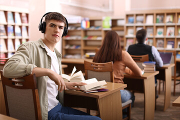 Man in headphones with books at desk in public library