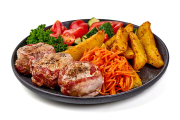 Grilled bacon-wrapped pork medallions with potato wedges, carrot salad, and fresh vegetables on a black plate, isolated on white background.