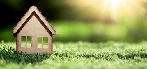 small wooden house model on grassy field with sunlit background creates serene atmosphere. sunlight enhances natural beauty of scene, evoking sense of tranquility