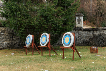 Three archery targets outdoors in a forested area with stone wall