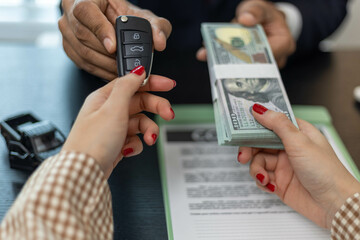 A man is giving a car key to a woman in exchange for a stack of green bills. The woman is holding the car key and the money in her hands
