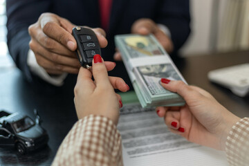 A man is giving a car key to a woman in exchange for a stack of green bills. The woman is holding the car key and the money in her hands
