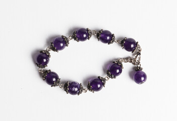 A bracelet of smooth round natural amethyst beads with silver clasp, on white background.