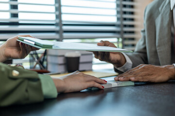 A man and a woman are sitting at a table with a judge. The man is handing the woman a piece of paper
