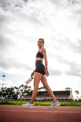 A focused female athlete captured during her training on the track, showcasing preparation, hydration, and determination in a vibrant stadium setting. Highlights fitness, motivation, and athletic perf