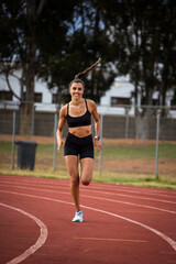 Obraz premium Female athlete in black sportswear training on a professional running track and running through various dynamic exercises, showcasing endurance, strength, and athleticism.