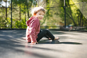 Fototapeta premium Little boy jumping on a trampoline in a backyard on warm and sunny summer day. Sports and exercises for children. Summer outdoor leisure activities.