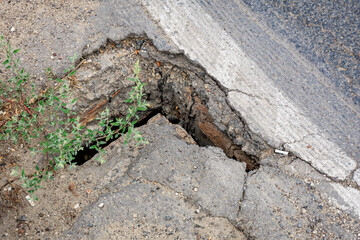 Cracked pavement with hole and weeds on asphalt road