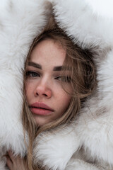 a close-up portrait of a blonde wrapped in a white fur coat