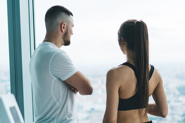 Back view of caucasian male and female athletes looking at window in moden gym dreaming about future,rear view of slim sportswoman and man talking to each other on break during training in active wear