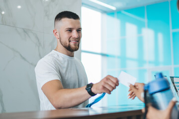 Handsome caucasian man receptionist in gym greeting female client giving key to access for...