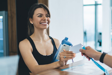 Happy caucasian female in active wear enjoying hospitable service in gym talking with male employee, cheerful 20s woman taking e-key access to locker room having friendly conversation with man