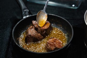small pieces of beef steak are fried in a frying pan, oil is poured onto the meat