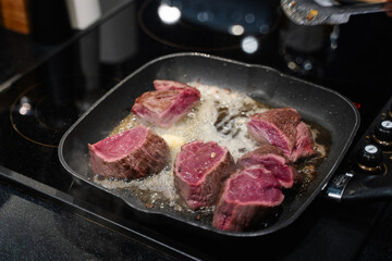 small pieces of beef steak are fried in a frying pan