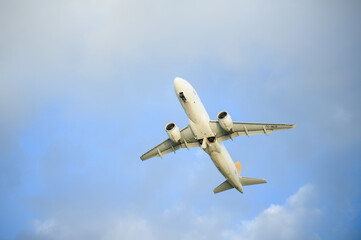 White passenger plane flying in blue sky, seen from below. Unmarked aircraft taking off or landing
