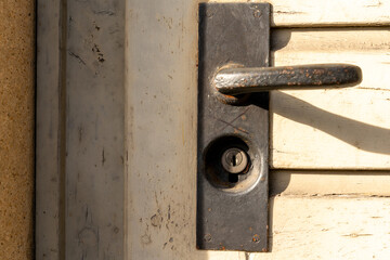 Old black door handle with some rust on a weathered wooden door.
