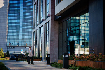 A young businesswoman in stylish attire walks along a modern city street. She appears confident and focused, embodying the essence of professional urban life. 