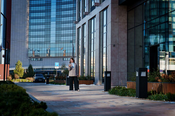 A young businesswoman in stylish attire walks along a modern city street. She appears confident and focused, embodying the essence of professional urban life. 