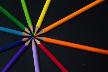 Naklejka premium Colored pencils arranged in circle on black background.