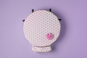 Robot vacuum wrapped in white polka dot gift paper with a pink bow on a pastel purple background. A creative and fun gift idea