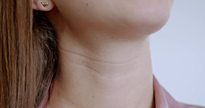 Close-up of a woman's neck and throat as she touches her skin. This video evokes themes of health, skincare, beauty, and wellness.
