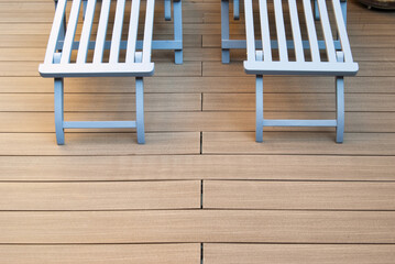  A pair of stylish light blue wooden lounge chairs with brass hinges and matching footrests are placed on a wooden deck. Holidays feeling.