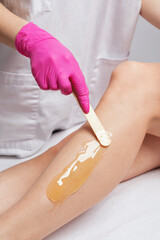 A beautician makes a sugar paste depilation of a woman's legs in a beauty salon. Female aesthetic cosmetology.