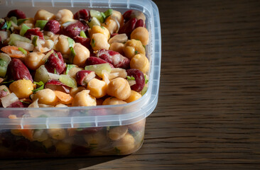 Close-up of a bean salad. Mix of chickpeas, kidney beans, and fresh veggies in a container.