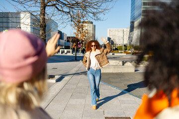 Stylish woman waving to friends while walking in a city square on a sunny day