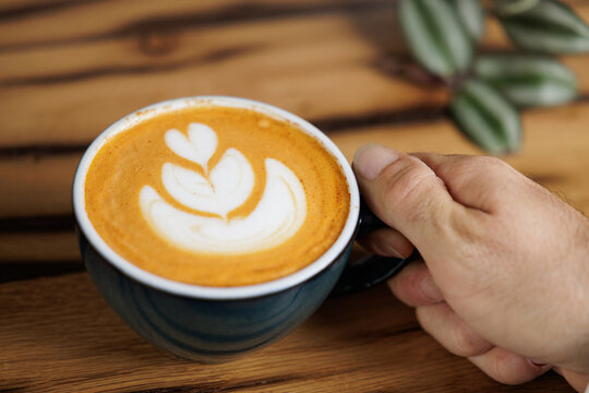 cup of specialty coffee with latte art in the shape of a flower in the hand of a young man. Copy space, close up