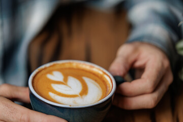 cup of specialty coffee with latte art in the shape of a flower in the hand of a young man. Copy space, close up