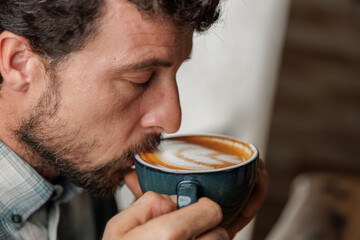 A young man enjoys a cup of specialty coffee with latte art to unwind from the work day. Copy space, close up.
