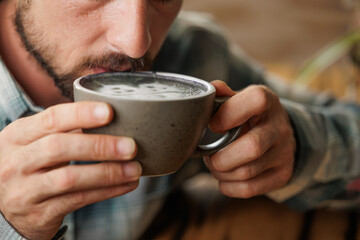 A young man enjoys a cup of specialty coffee with latte art to unwind from the work day. Copy space, close up.