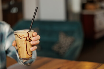A happy and close young man smiling in an iced coffee with caramel, decoration with plants, cold and refreshing drink.