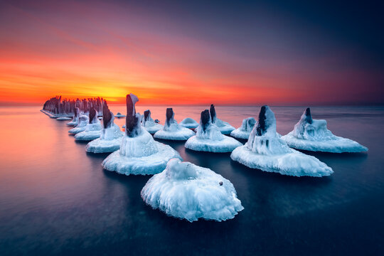 Wooden posts of an old pier covered in ice in Baltic Sea at sunset, Sventoji, Lithuania