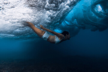 Woman duck dive with out surfboard under breaking ocean wave.