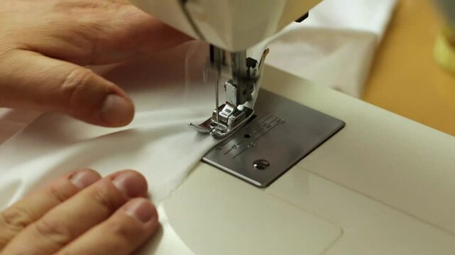 cosiendo una tela blanca en una m&aacute;quina de coser el&eacute;ctrica, trabajo desde casa