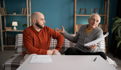 worried senior father with his son checking bills and expenses at home, debt, taxes and home budget