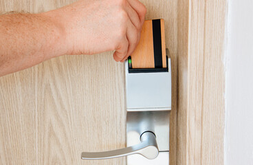 Man hotel guest using wood key card to unlock hotel room door in eco friendly green sustainable...