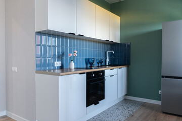 design of modern small kitchen. built-in kitchen with white cabinets, blue tile backsplash, wooden...
