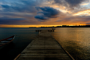 Obraz premium Sunset on a wooden pier. Wooden fishing boats. Fishermen's nets. Sunset over the sea. Dark sunset. Calm sea