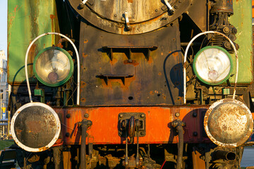 an old historic coal-fired steam locomotive standing as an exhibit at the railway station. rusty metal. classic train lamps with reflectors, train bumpers and steam boiler.