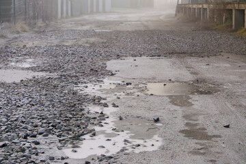 road during morning fog. Bad weather conditions while driving will occur in autumn and winter. poor visibility on the road. ice on the road. frozen puddles on the access road covered with stones