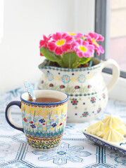 Ceramic mugs with a yellow floral pattern with a yellow floral pattern. There is flowers in a jug in the background. Selective focus. 