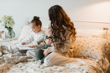 Smiling young woman sitting in bed with her young daughter and son reading a book