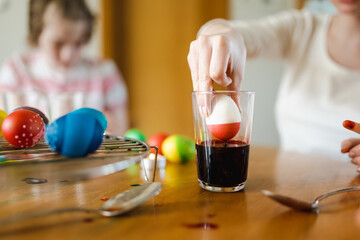 Pretty teenage girl dyeing Easter eggs at home. Child painting colorful eggs for Easter hunt. Kid getting ready for Easter celebration.
