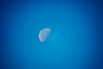 A clear view of the moon in a vibrant blue sky, showcasing its craters and details during daylight hours