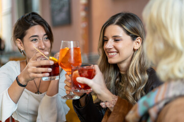 Three young women toasting with cocktails at a trendy bar during a night out - happy our drink celebration